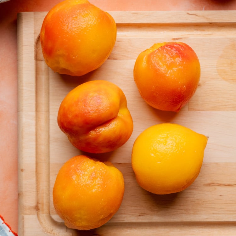 Five peaches on a cutting board after blanching and removing the skin.