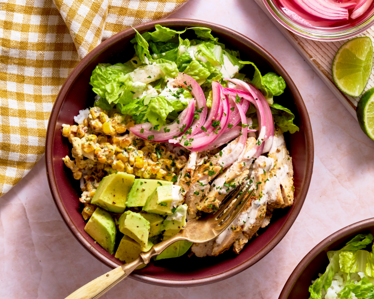 Street corn bowl assembled and topped with lettuce, pickled onions, chipotle crema, and avocado.