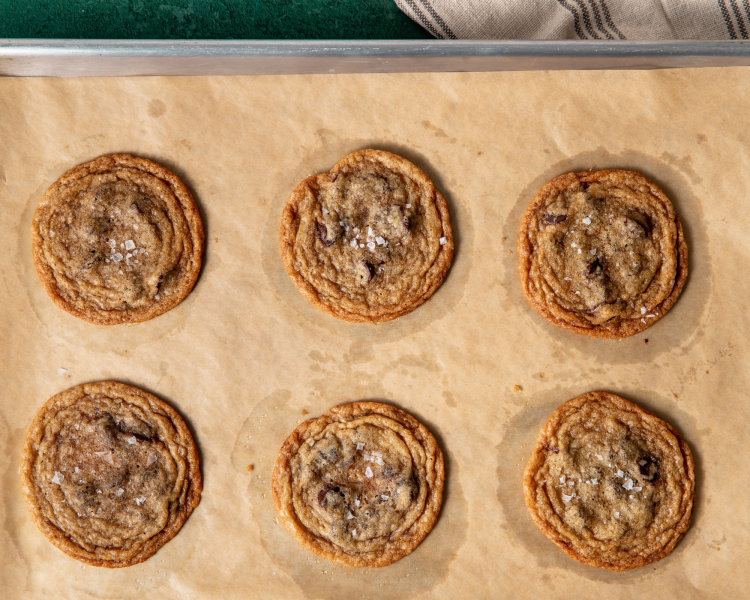 Six tate's bake shop chocolate chip cookies baked on parchment-lined baking sheet.