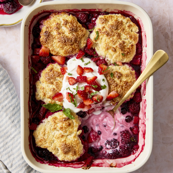 Mixed berry cobbler baked in ceramic baking dish with one biscuit in the bottom right corner scopped out.