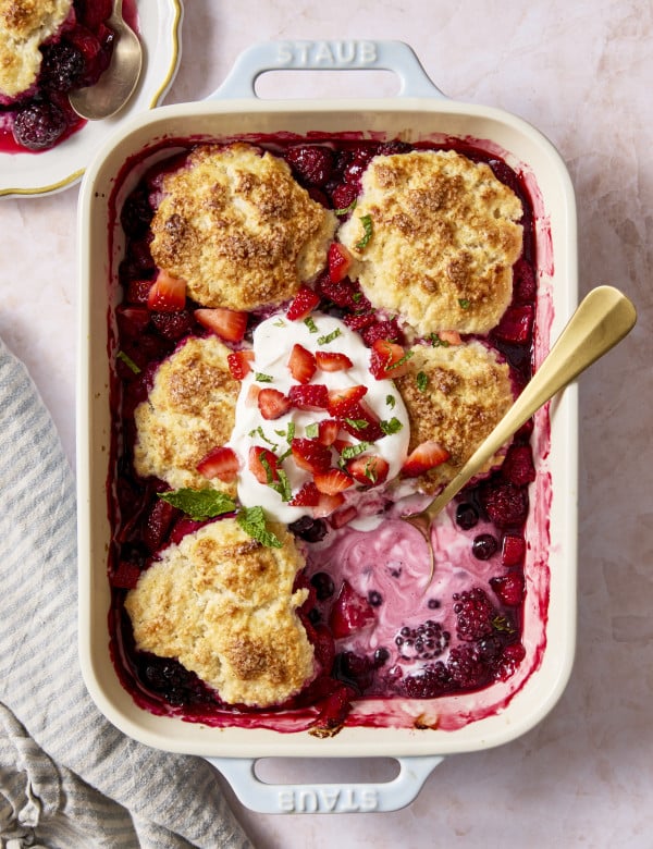 Mixed berry cobbler baked in ceramic baking dish with one biscuit in the bottom right corner scopped out.