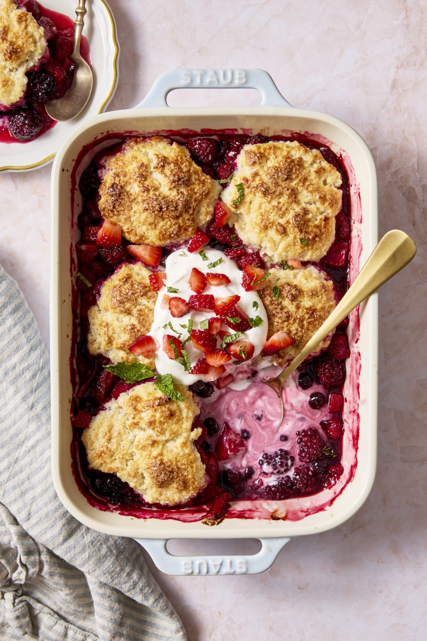 Mixed berry cobbler baked in ceramic baking dish with one biscuit in the bottom right corner scopped out.