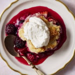 Mixed berry cobbler served on a plate with fresh whipped cream on top.