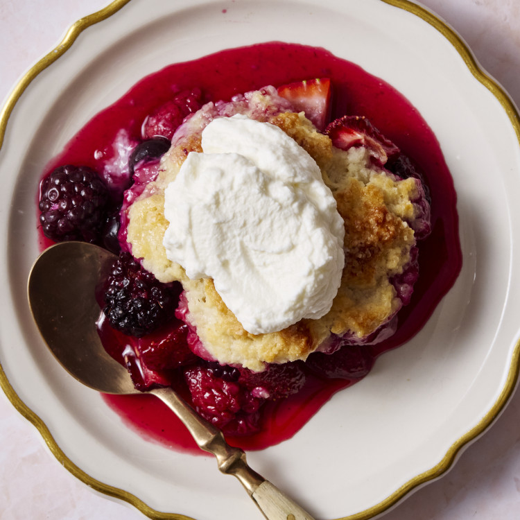 Mixed berry cobbler served on a plate with fresh whipped cream on top.