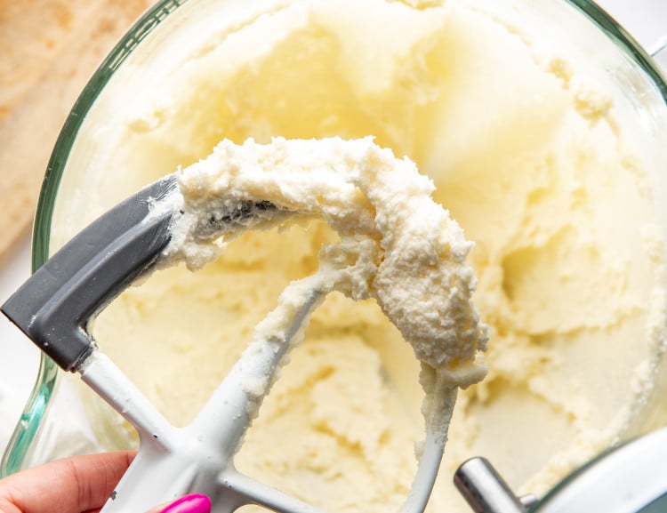 Hand holding paddle attachment showing creamed butter and sugar on it.