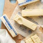 Several sticks of butter softened on wood cutting board with one stick showing indention.