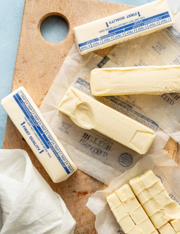 Several sticks of butter softened on wood cutting board with one stick showing indention.