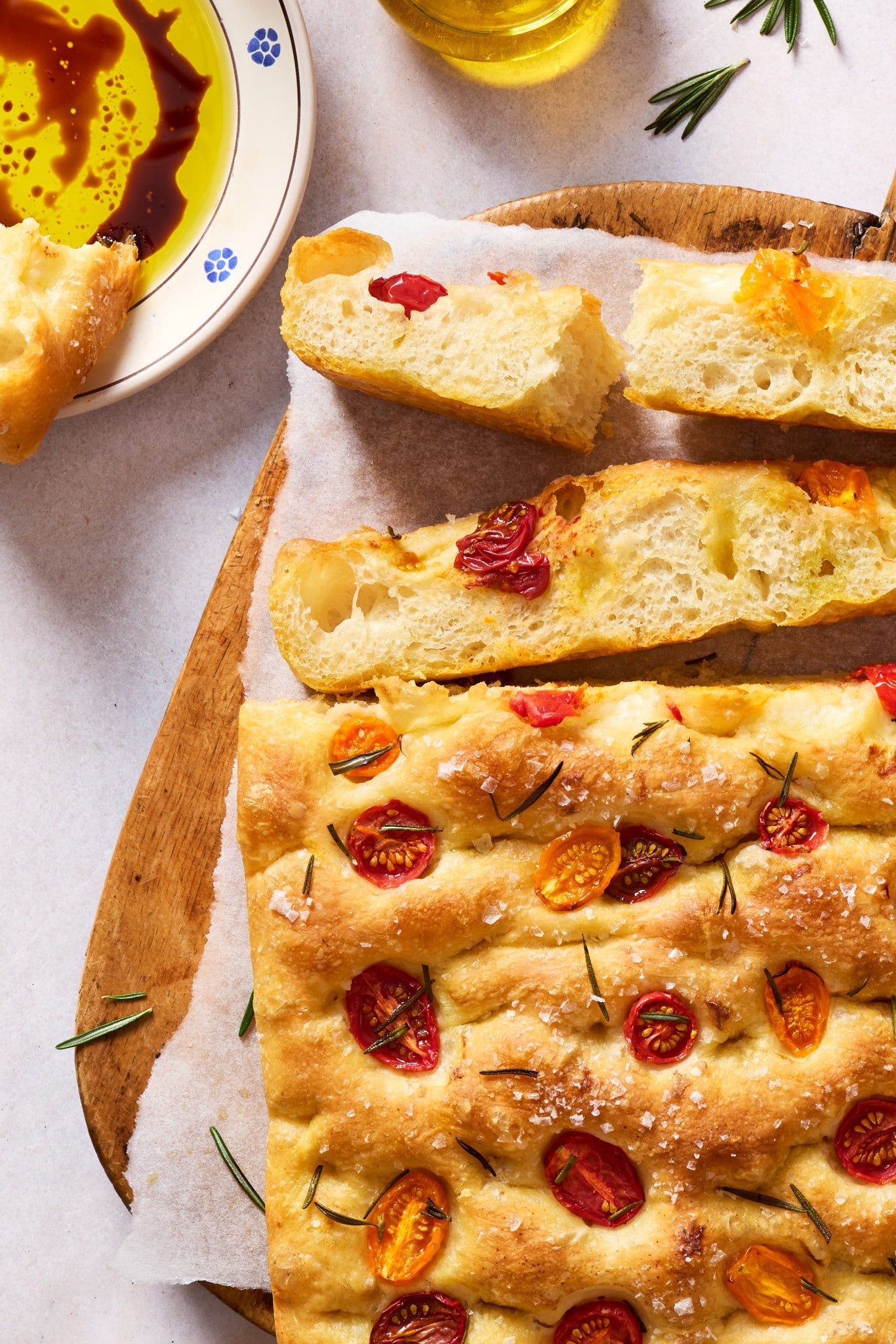 Close-up of sliced tomato rosemary focaccia with a crisp golden crust, fluffy interior, flaky sea salt, and olive oil dipping sauce.