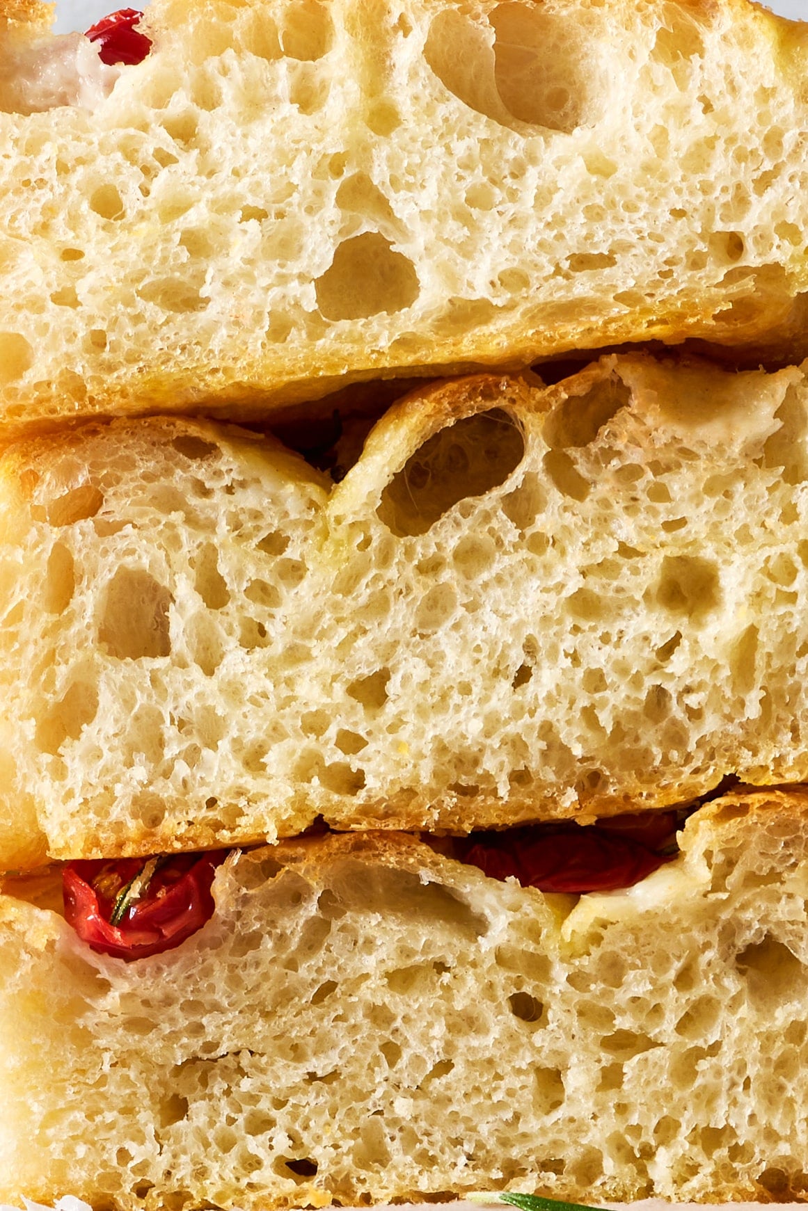 Extreme close-up of tomato rosemary focaccia highlighting the soft, airy crumb, large air pockets, and golden, crisp crust.
