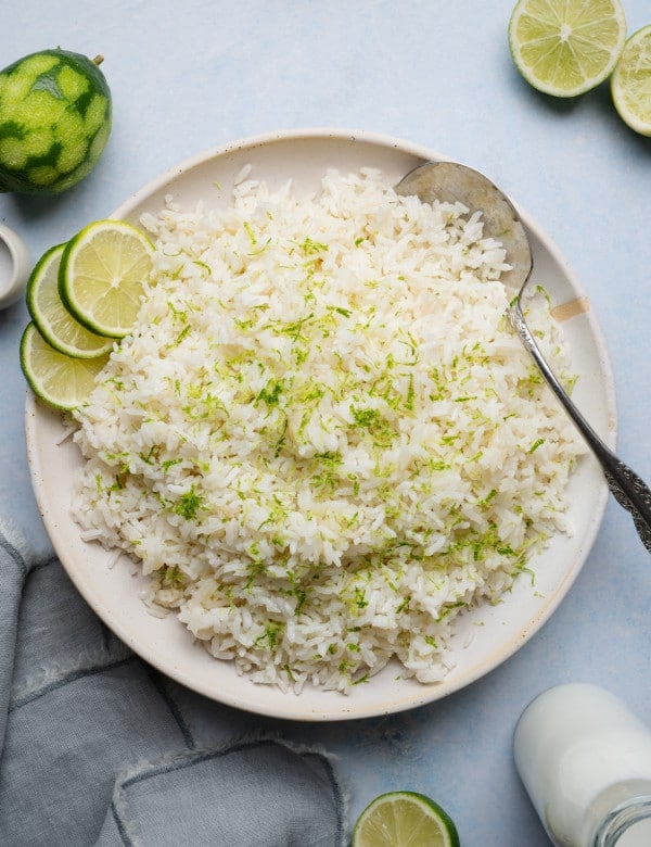 Coconut lime rice served on a plate garnished with fresh lime zest and serving spoon on the side.