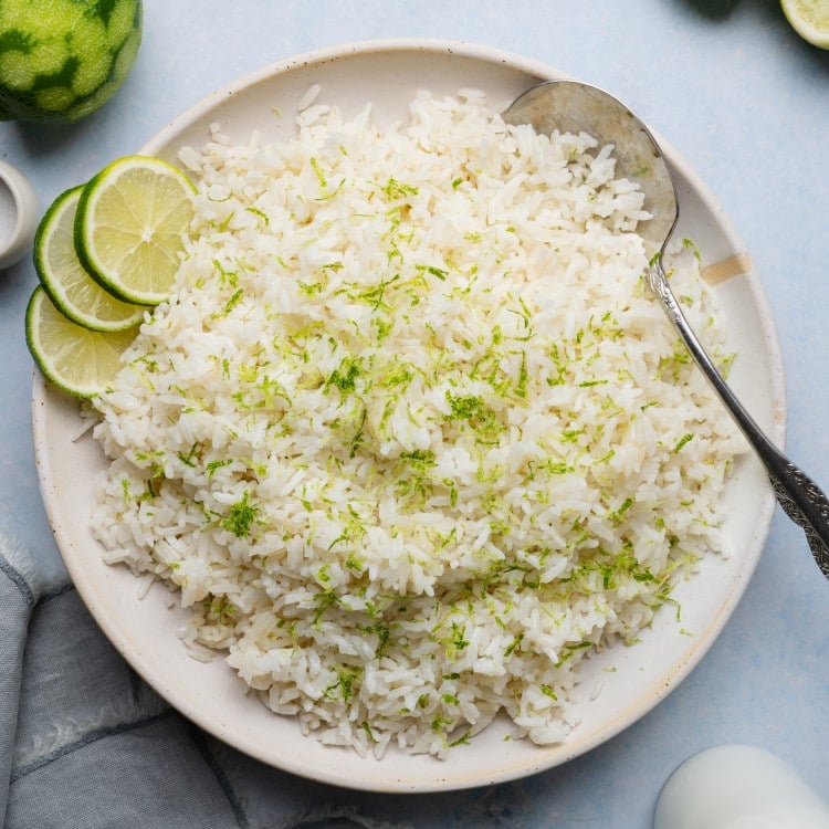 Coconut lime rice served on a plate garnished with fresh lime zest and serving spoon on the side.