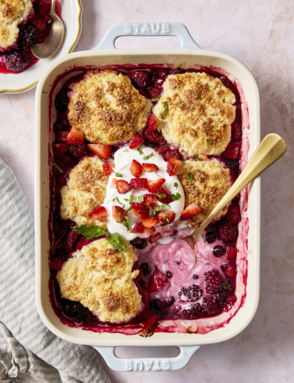 Mixed berry cobbler baked in ceramic baking dish with one biscuit in the bottom right corner scopped out.