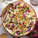 Crunchy asian slaw in a large mixing bowl with two wooden spoons on the side.