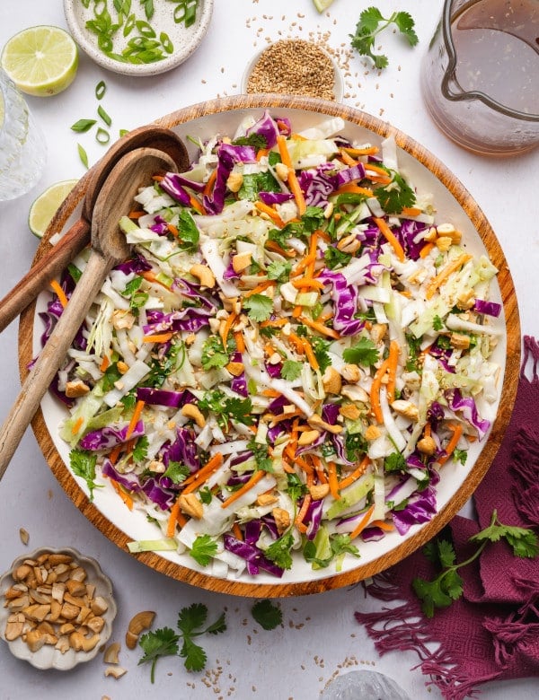 Crunchy asian slaw in a large mixing bowl with two wooden spoons on the side.
