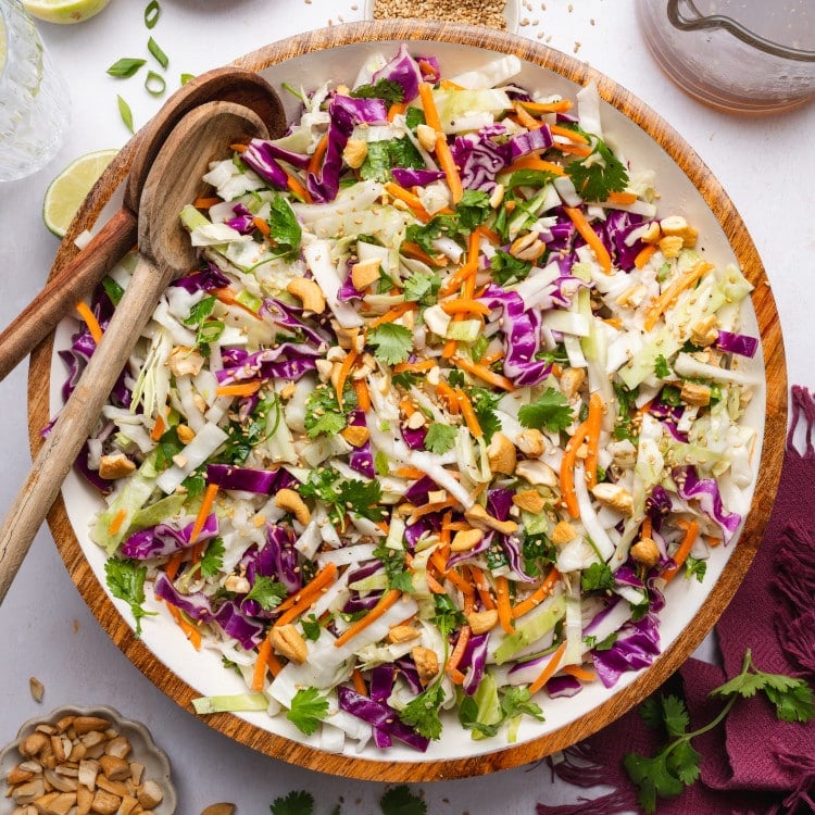 Crunchy asian slaw in a large mixing bowl with two wooden spoons on the side.