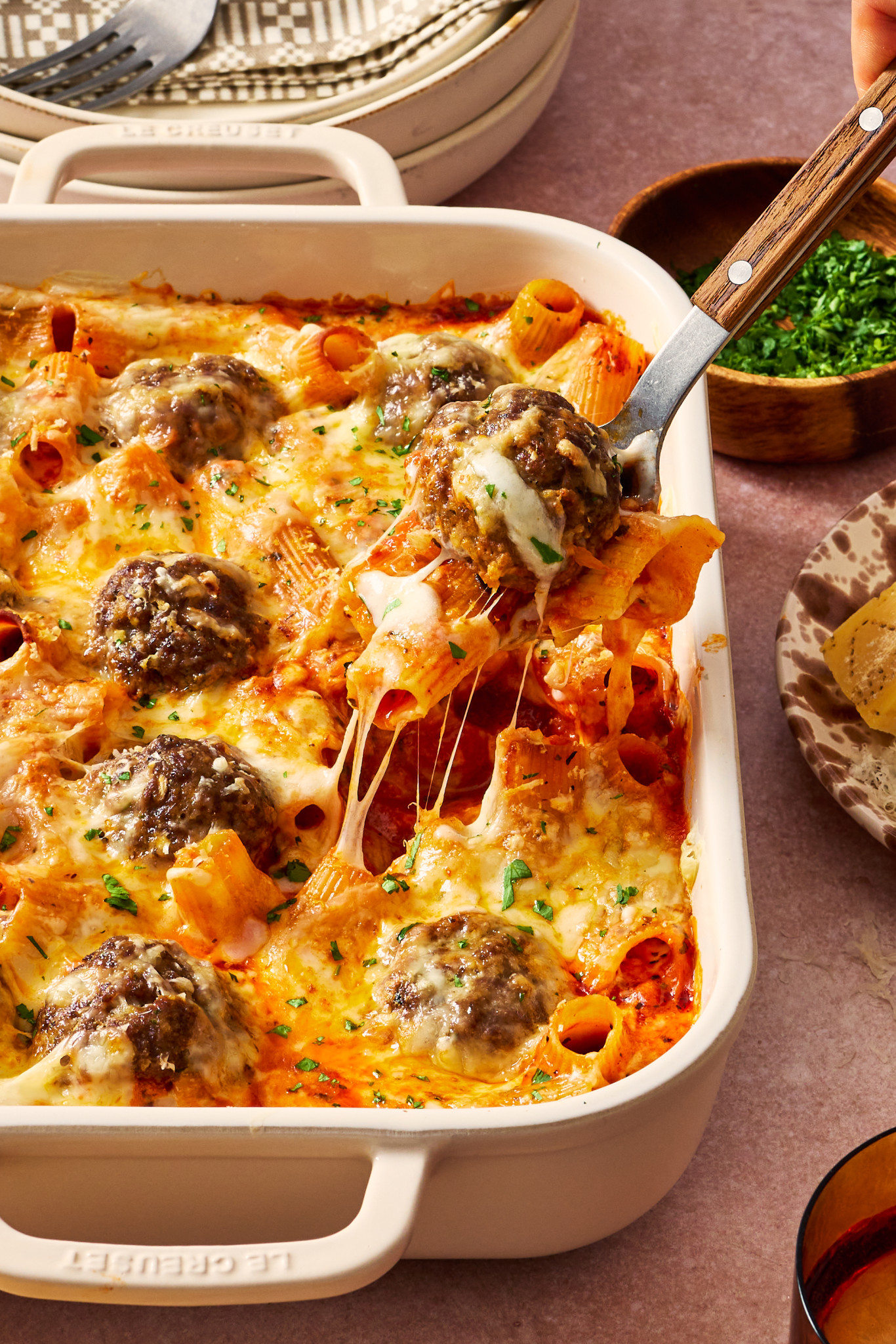 Fork scooping out pasta and meatball from bake in casserole dish.