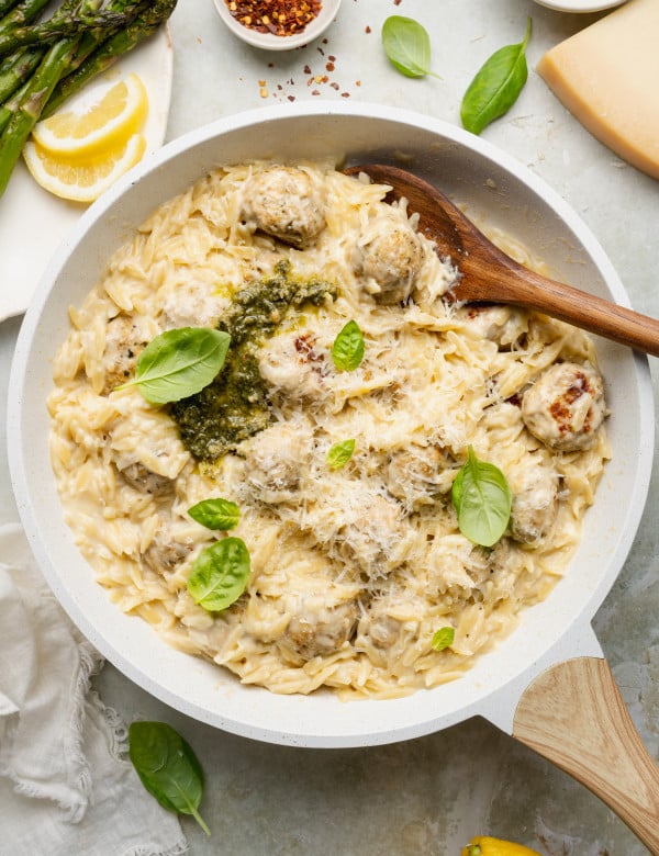 Pesto chicken meatballs and orzo cooked in skillet and topped with extra basil, pesto and parmesan cheese.