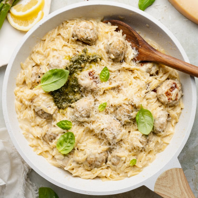 Pesto chicken meatballs and orzo cooked in skillet and topped with extra basil, pesto and parmesan cheese.