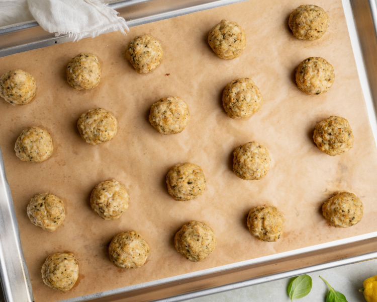 Cooked pesto chicken meatballs on a parchment-lined baking sheet.