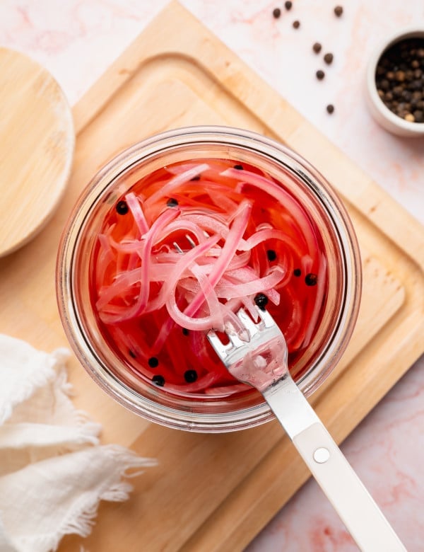 Fork lifting pickled onions out of jar.