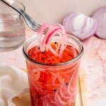 Fork lifting onions out of large glass jar.