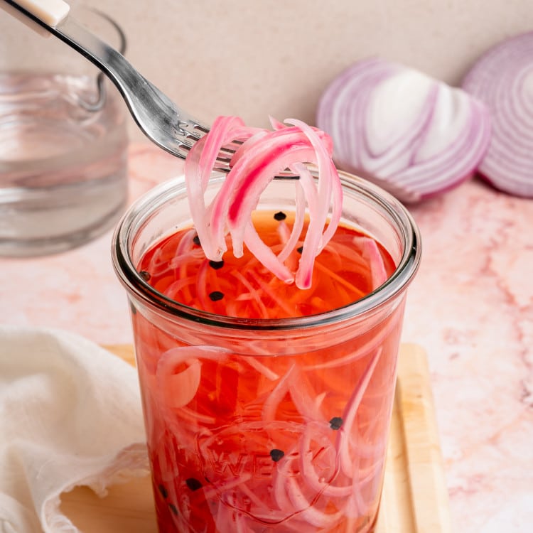 Fork lifting onions out of large glass jar.