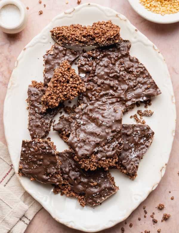Pieces of chocolate covered quinoa bark on white oval serving platter.