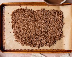 Chocolate covered quinoa spread out on parchment-lined baking sheet.