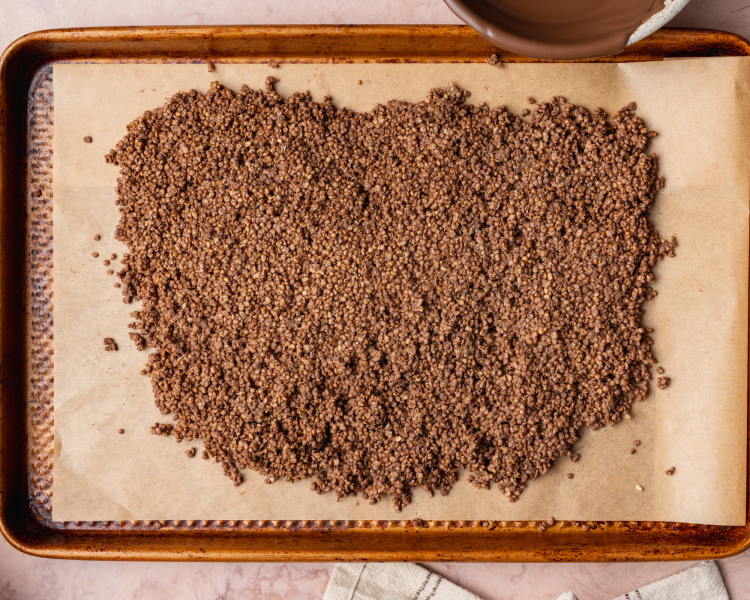Chocolate covered quinoa spread out on parchment-lined baking sheet.