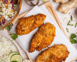 Transferring cooked chicken to paper-towel lined plate to soak up excess oil.