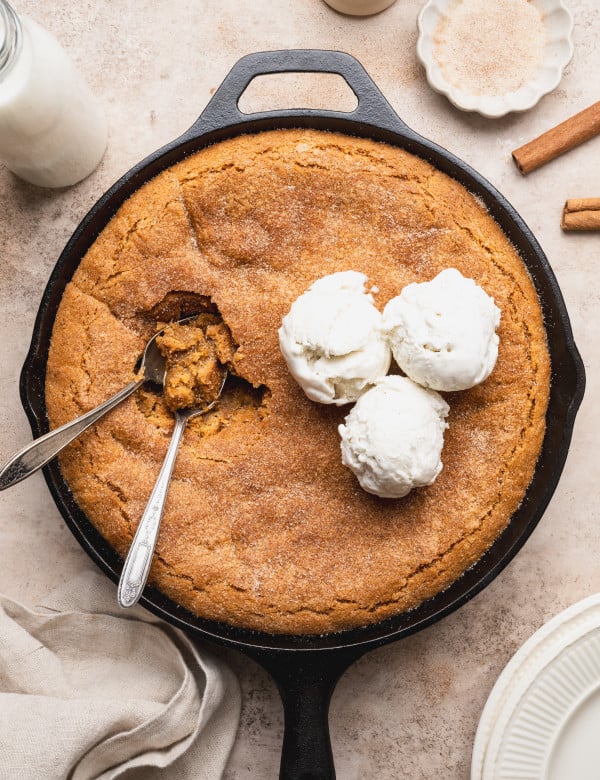 Snickerdoodle cookie skillet topped with three scoops of vanilla ice cream with two spoons digging in.