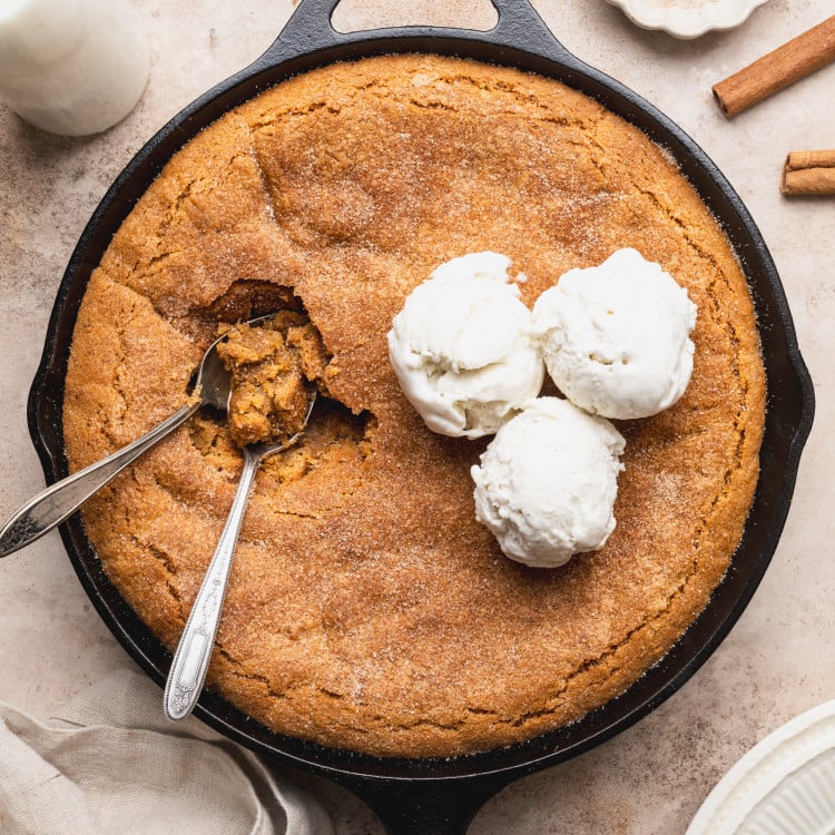Snickerdoodle cookie skillet topped with three scoops of vanilla ice cream with two spoons digging in.