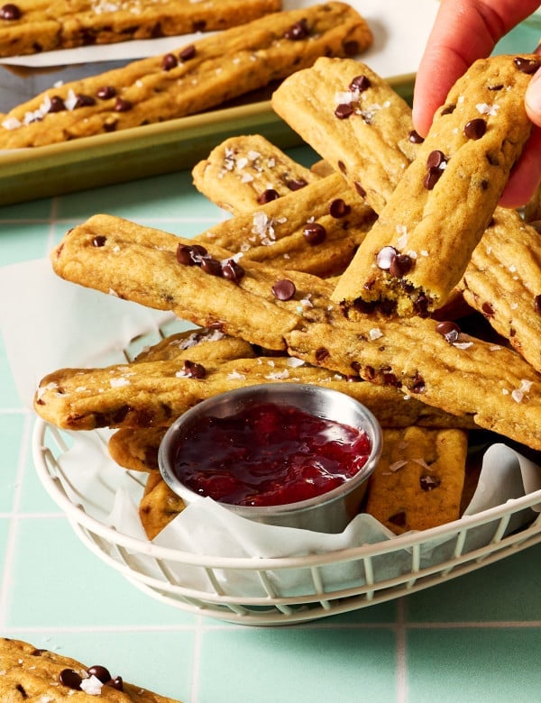 Hand holding half a cookie fry being dip in strawberry syrup.