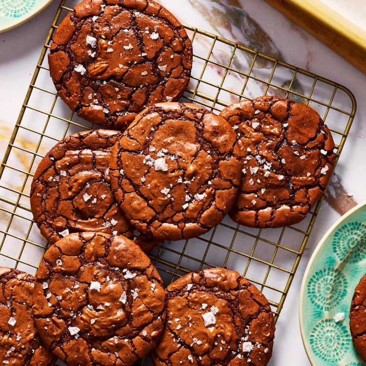 Crackly top brownie cookies on top of cooling rack sprinkled with flaky salt.