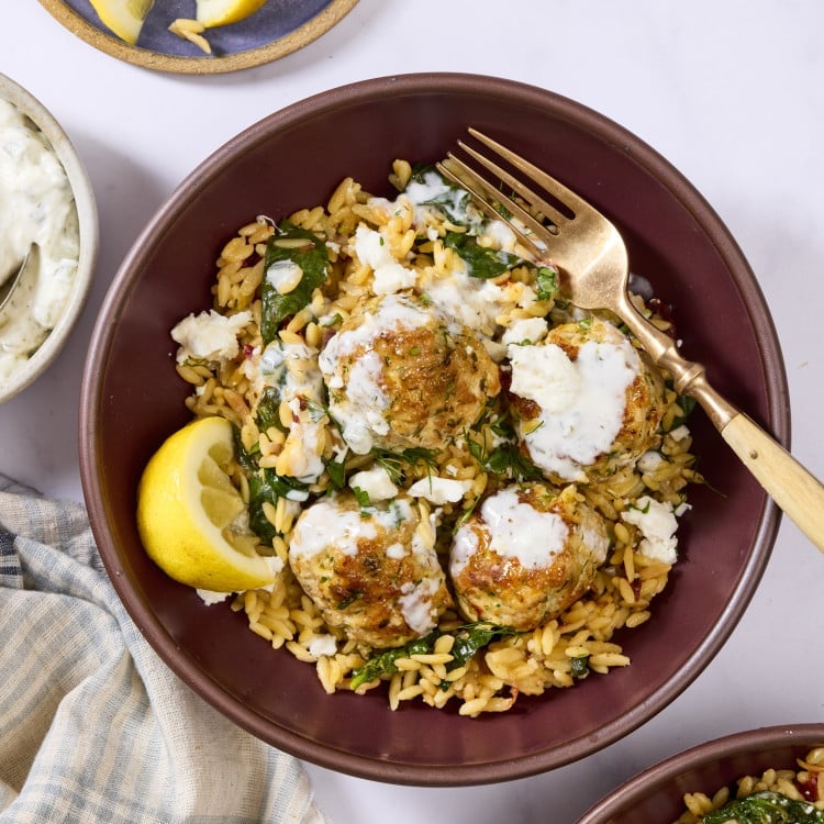 Mediterranean meatball and orzo in bowl topped with tzatziki and lemon wedge.