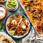Two tortillas filled with steak fajitas on a plate and topped with sour cream and pico de gallo.