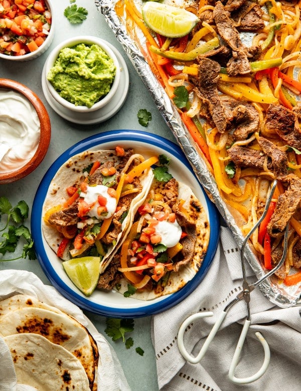 Two tortillas filled with steak fajitas on a plate and topped with sour cream and pico de gallo.