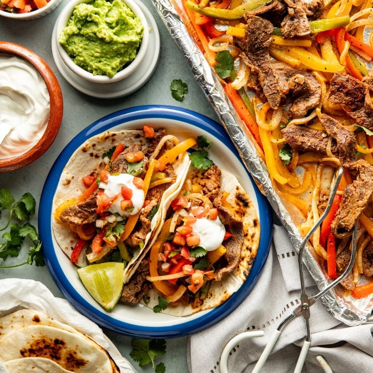 Two tortillas filled with steak fajitas on a plate and topped with sour cream and pico de gallo.
