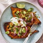 Two sweet potato halves topped with ground turkey, avocado, sour cream, pickled red onions and cilantro on a plate with a fork.