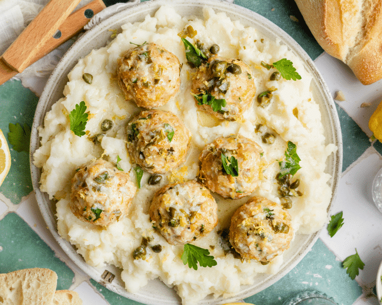 Chicken piccata meatballs served on top of plate with mashed potatoes.