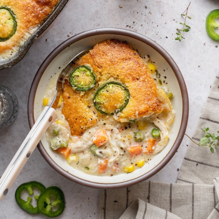 Serving of cornbread chicken pot pie scooped into a bowl with spoon on the side.