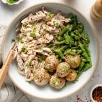 Slow cooker garlic ranch chicken served in a bowl with green beans and yukon gold potatoes in a bowl with fresh parsley and red pepper flakes.