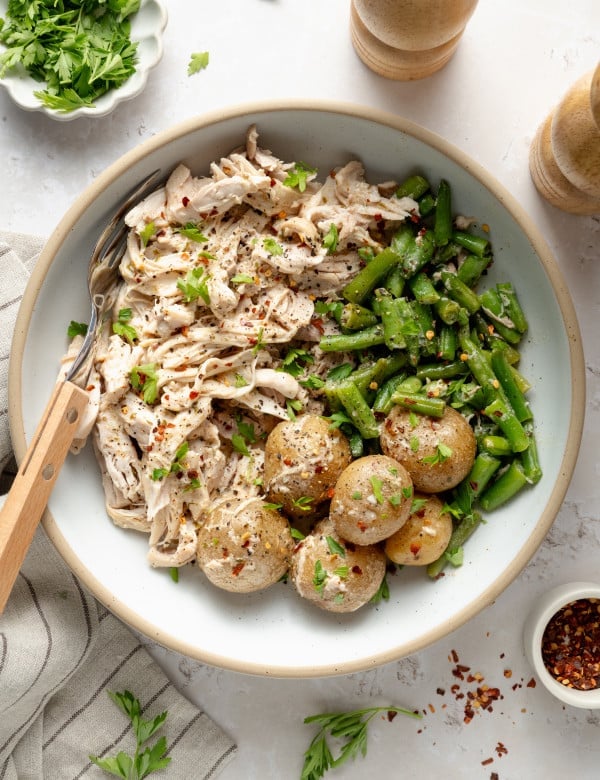 Slow cooker garlic ranch chicken served in a bowl with green beans and yukon gold potatoes in a bowl with fresh parsley and red pepper flakes.