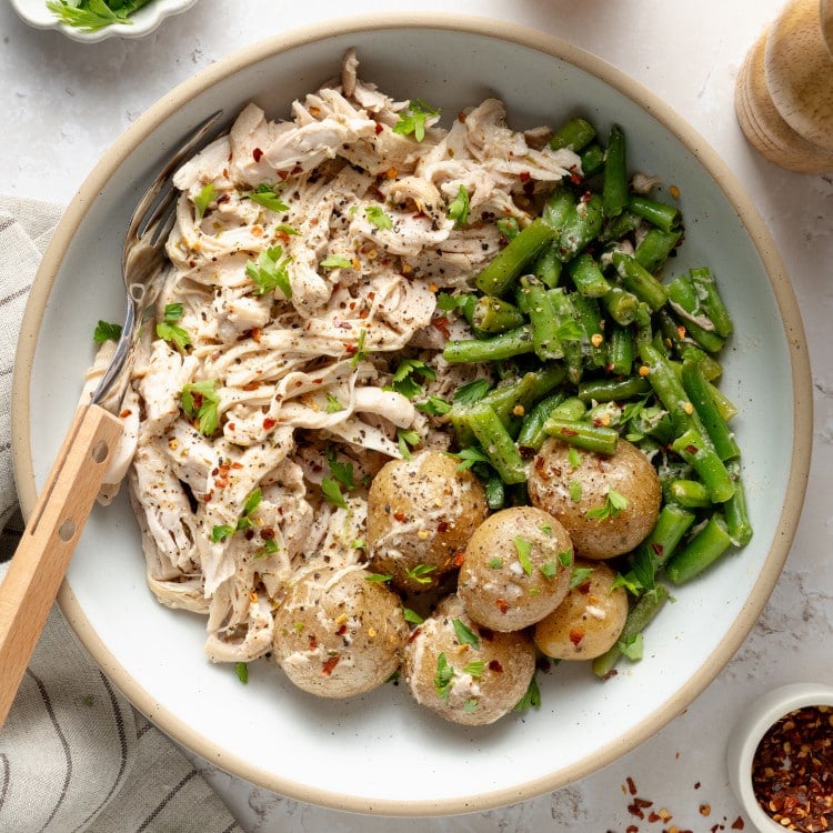 Slow cooker garlic ranch chicken served in a bowl with green beans and yukon gold potatoes in a bowl with fresh parsley and red pepper flakes.