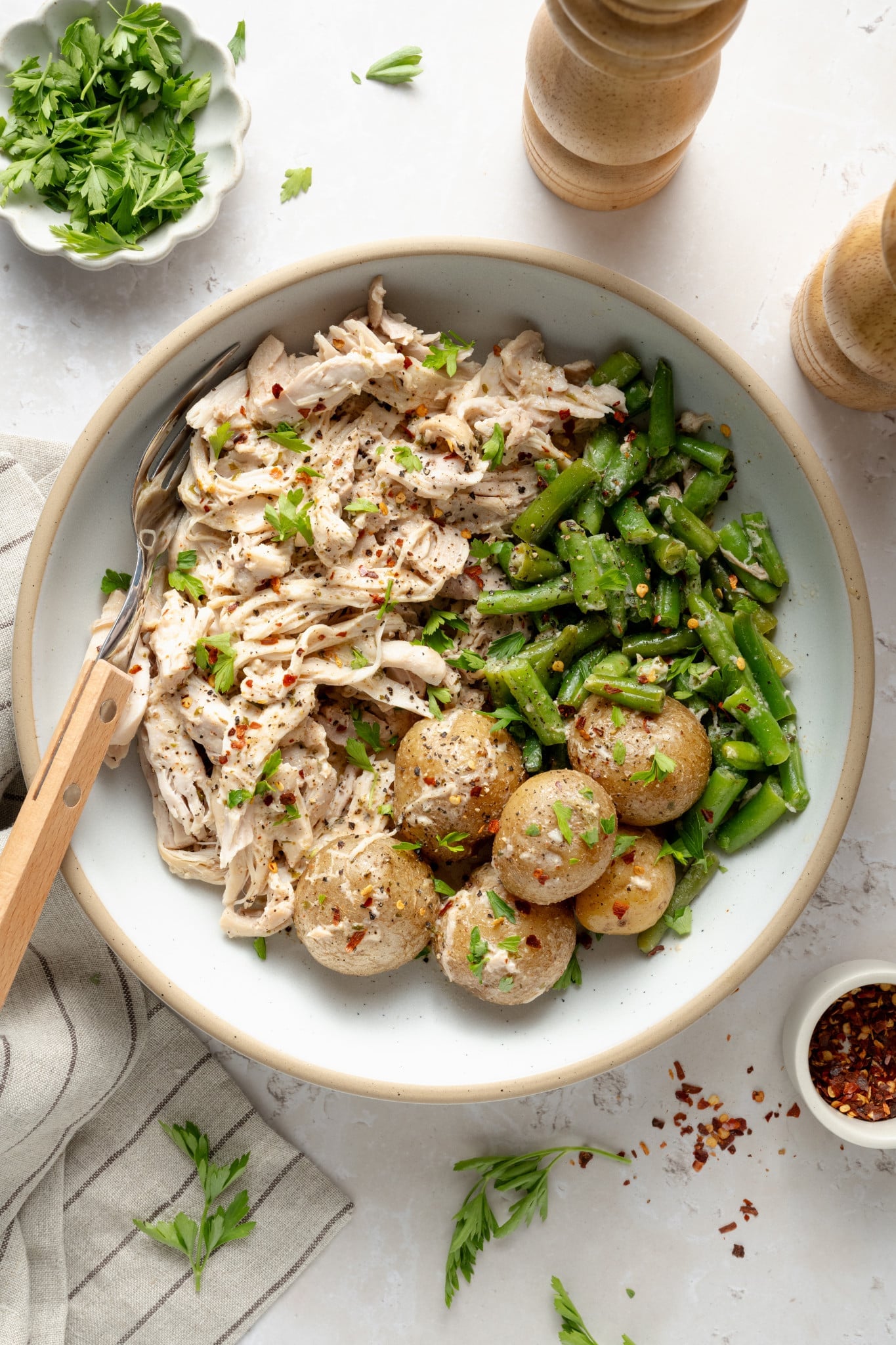 Slow cooker garlic ranch chicken served in a bowl with green beans and yukon gold potatoes in a bowl with fresh parsley and red pepper flakes.