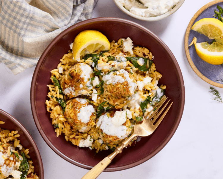 Cooked meatballs and orzo served in a bowl then topped with tzatziki and a lemon wedge.