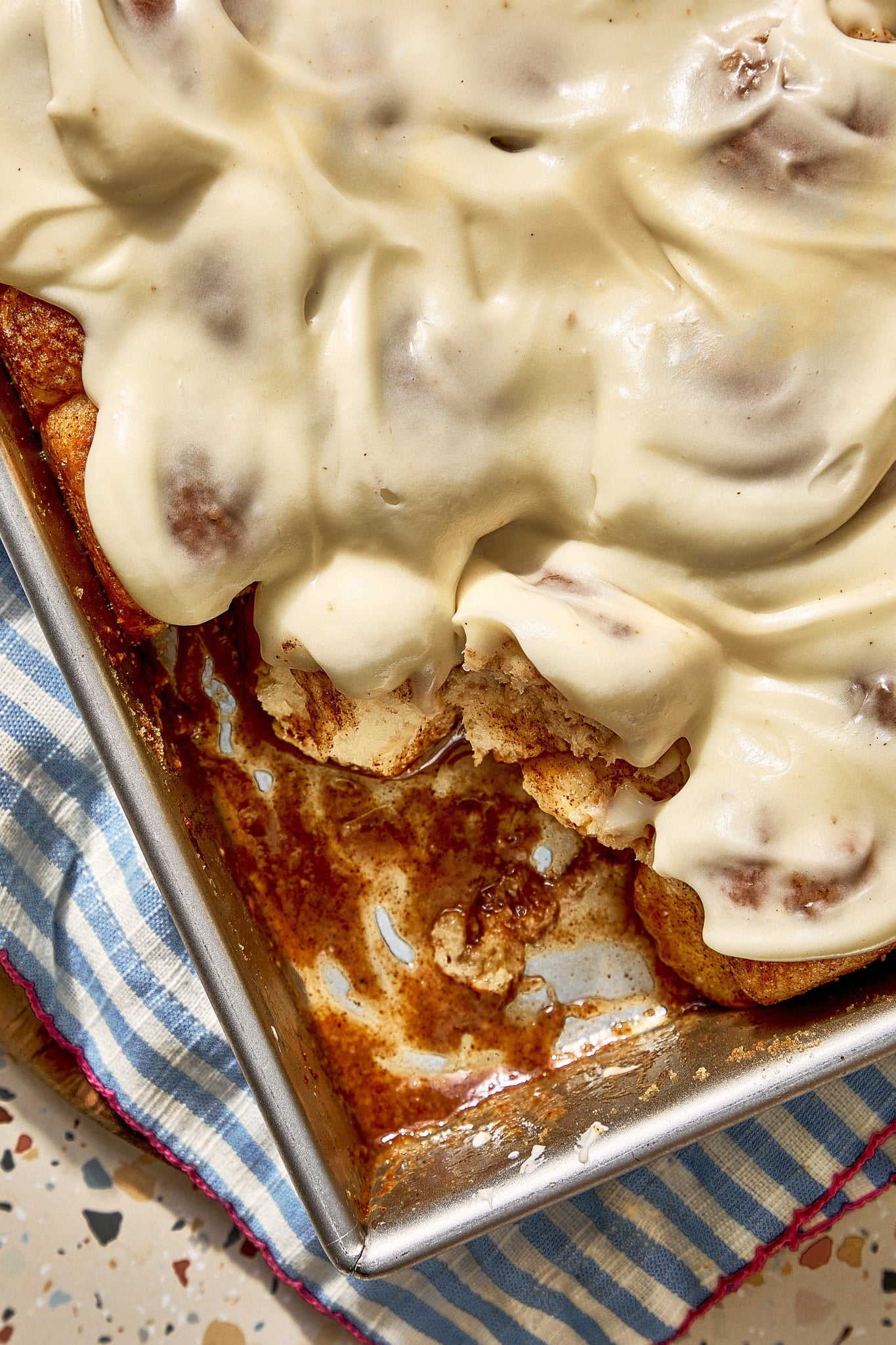 Close-up of frosted cinnamon roll bites pulled from the pan, showing their soft centers and gooey cinnamon sugar sauce underneath.
