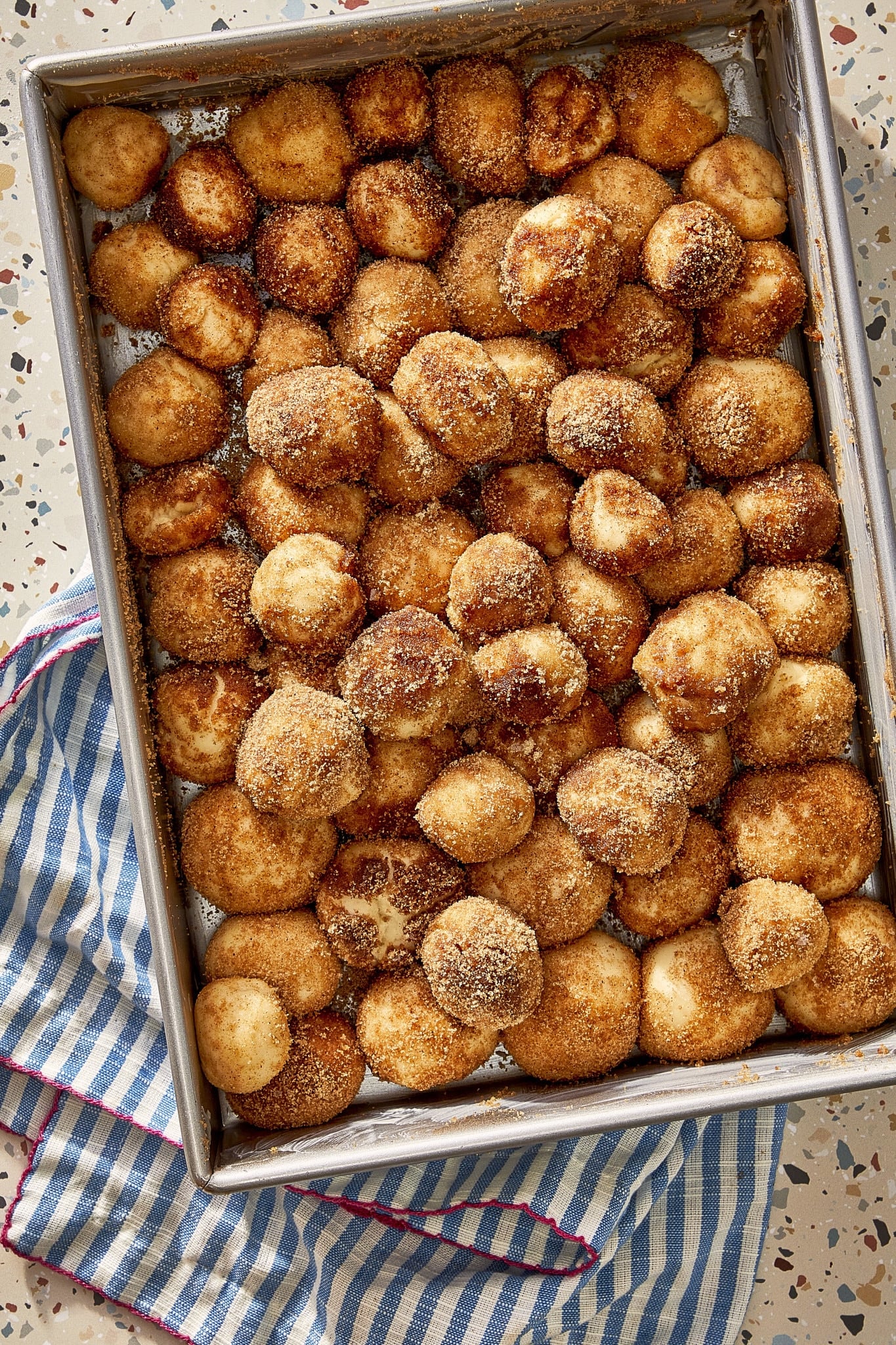 Small balls of cinnamon roll dough coated in melted butter and cinnamon sugar and arranged in a baking pan.