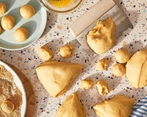 Risen cinnamon roll dough divided into portions and rolled into small balls before coating with butter and cinnamon sugar.