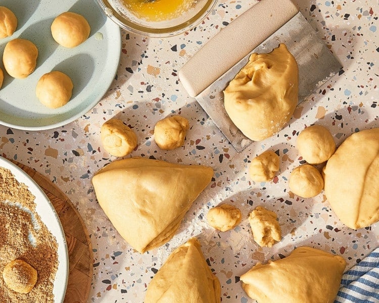Risen cinnamon roll dough divided into portions and rolled into small balls before coating with butter and cinnamon sugar.